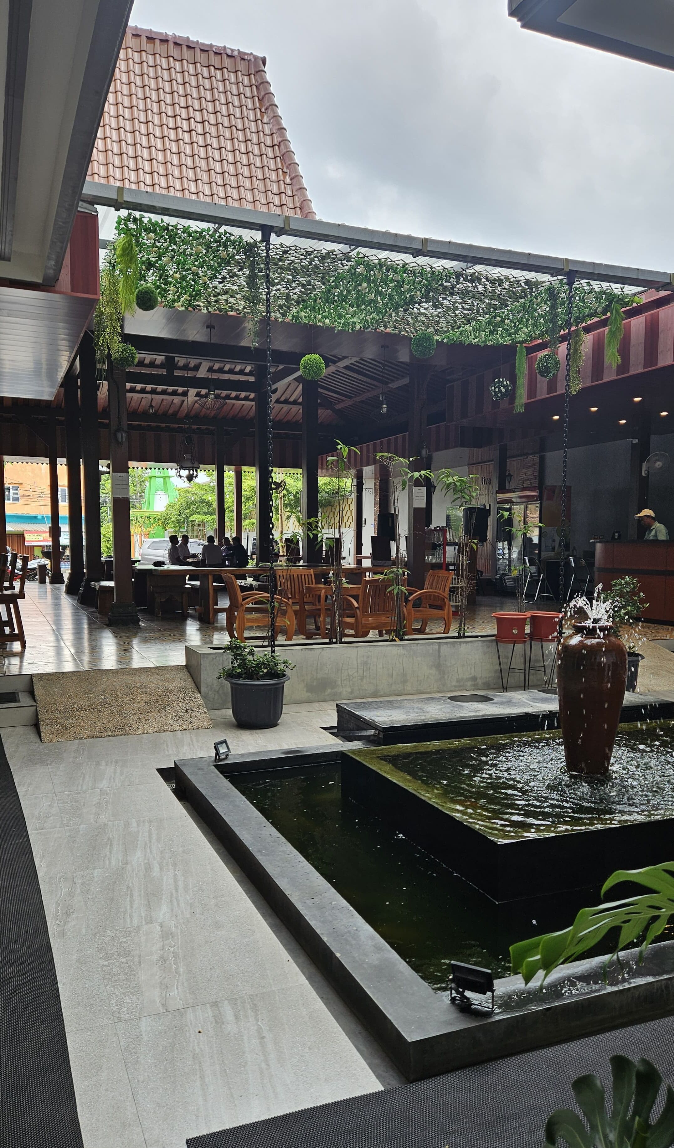 A covered outdoor seating area with tables and chairs, a small water feature, and potted plants.
