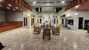 Um hall amplo com área de estar central, pisos com ladrilhos estampados e teto alto com vigas aparentes.