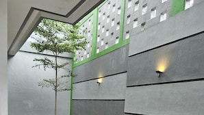 Um jardim interno moderno com um caminho de pedra, uma árvore e uma parede com detalhes verdes e luminárias.