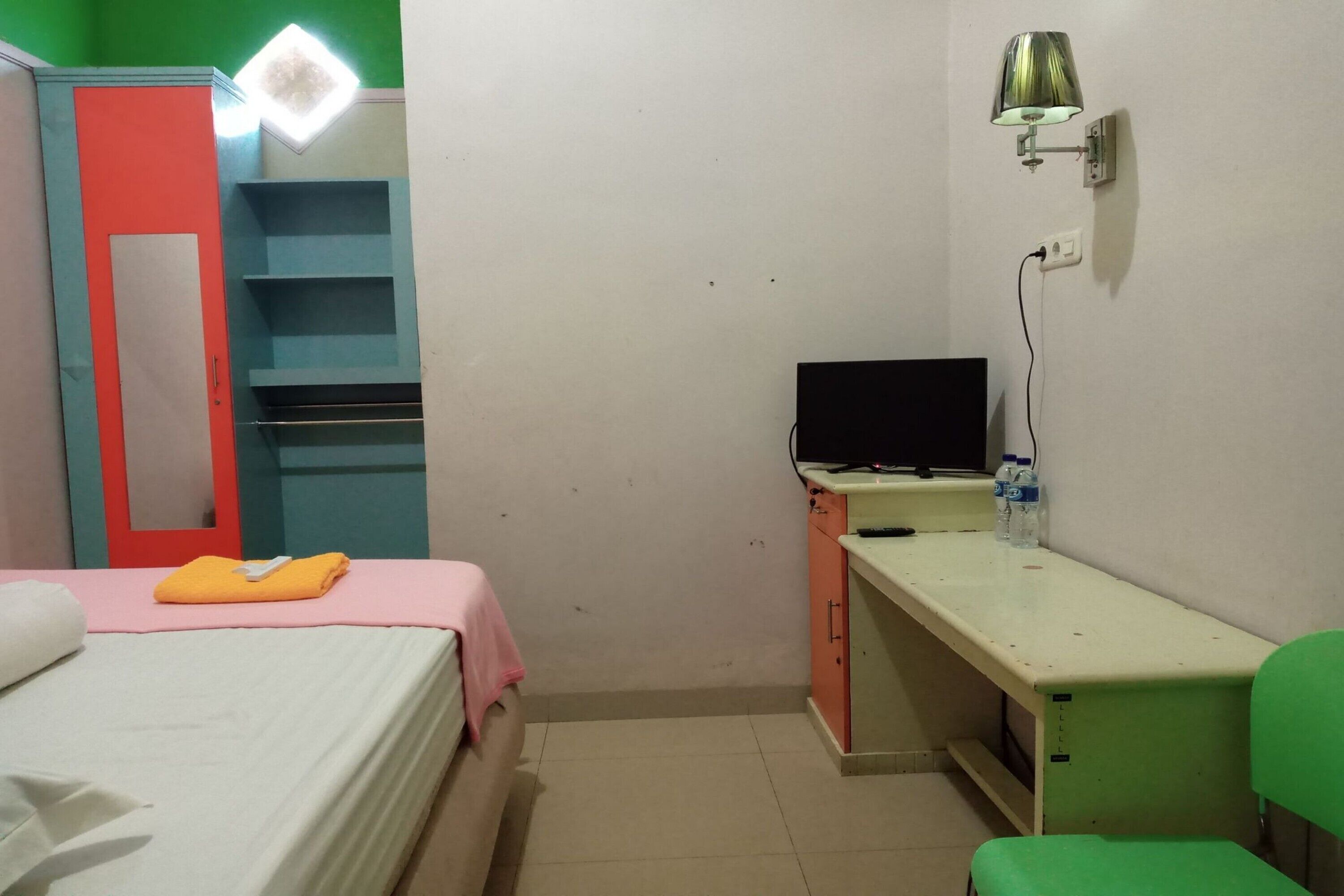 A small, compact room with a bed, a desk, a chair, a TV, and a wardrobe.