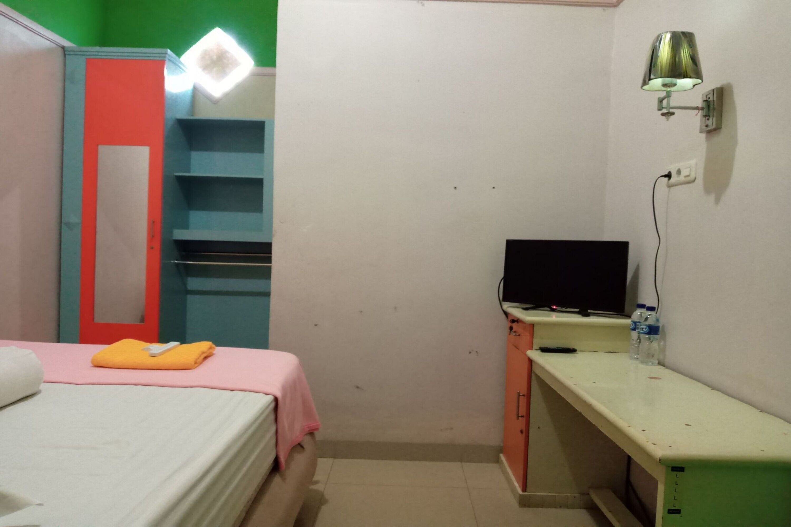 A small, neatly organized bedroom with a bed, a desk, a TV, and a wardrobe.