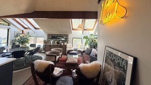 Un amplio espacio habitable con techo alto, tragaluces, un letrero de neón y una zona de comedor con sillas y una mesa.