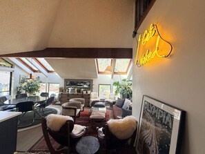 Un'ampia zona giorno con soffitto alto, lucernari, un'insegna luminosa e un'area pranzo con sedie e tavolo.