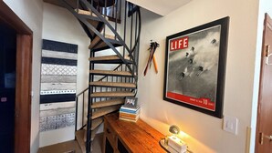 Una escalera con acabado de madera, un póster enmarcado en la pared y una pequeña mesa con una vela y un objeto decorativo.
