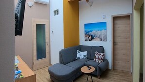 Una sala de estar acogedora con un sofá seccional gris, una mesita redonda y un televisor montado.