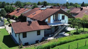 Una casa de dos pisos con un balcón, rodeada por un césped cuidado y un paisaje montañoso.
