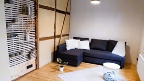 Ein Zimmer mit Holzboden, einem dunkelgrauen Sofa, einer weißen Wand und einer hängenden Leuchte.