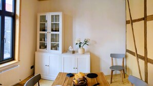 Ein Zimmer mit Holzboden, einem weißen Schrank mit Glastüren, einem Esstisch mit Stühlen und einem Fenster mit Blick.