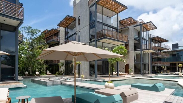 Et moderne resort med en stor udendørs pool, flere balkonniveauer og udendørs siddeområder.
