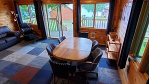 Une cabane en bois avec une grande table à manger et des chaises, un canapé et une petite table sur laquelle se trouve un panier.