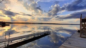 Un lac paisible, avec une jetée en bois qui s’avance sur l’eau, le tout baigné d’un ciel dégagé.