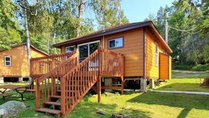Een houten chalet met een trap naar een terras, omringd door gras en bomen.