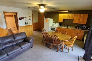 A compact living space with a dining table and chairs, a sofa, a kitchen area with wooden cabinets, and a ceiling fan.