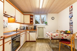 A kitchen with wooden cabinets, a microwave, a sink, and a dining table with a red and white tablecloth. - Apartment 'Berghansenhof' with Mountain View, Private Terrace and Wi-Fi (Wolfach)