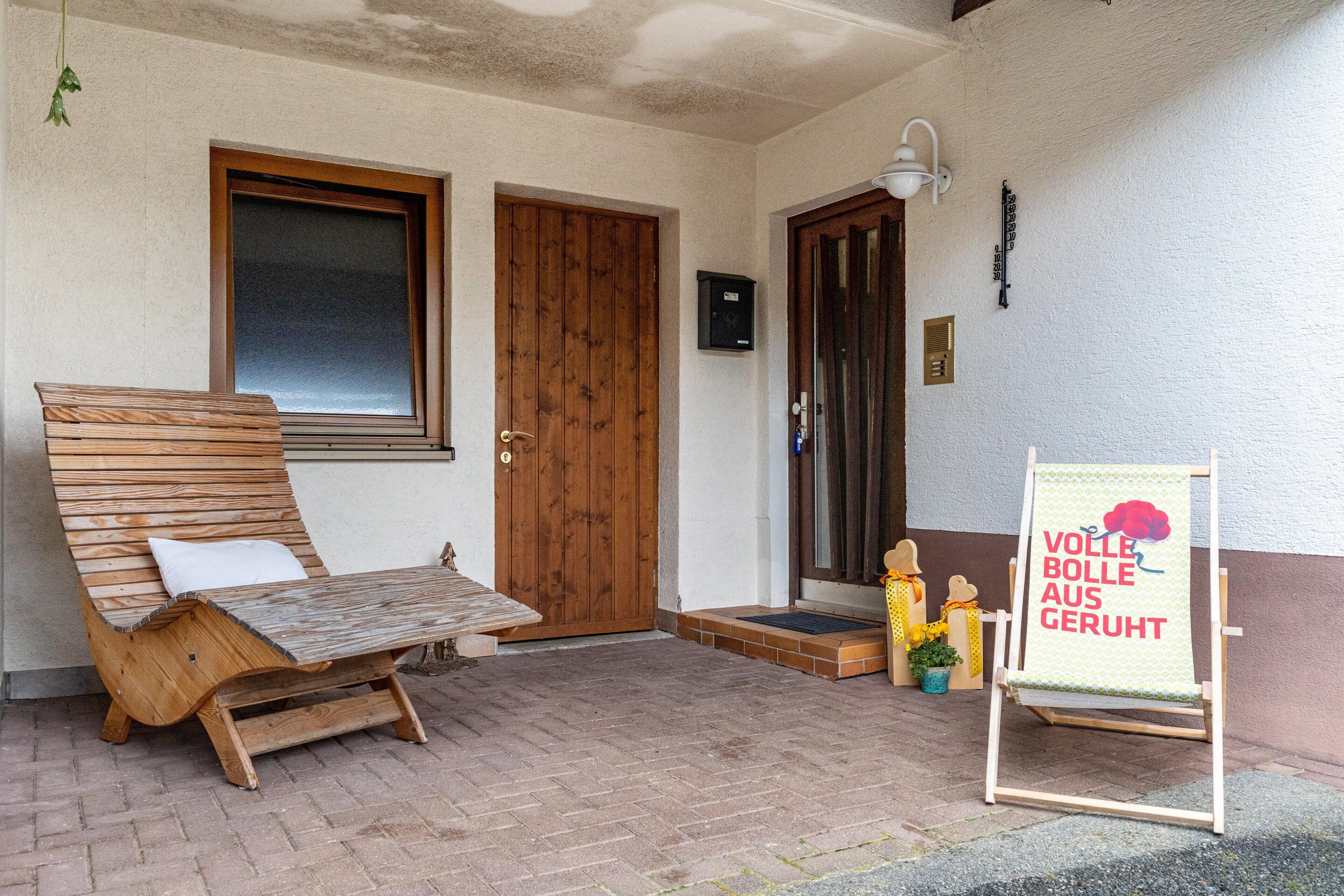 Eine hölzerne Bank, eine Tür, ein an der Wand befestigtes Schild und ein kleiner Topfpflanze.