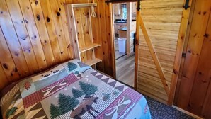 Ein Holzhütten-Innenraum mit Bett, Kleiderstange und einer Tür zu einer Küchenzeile.
