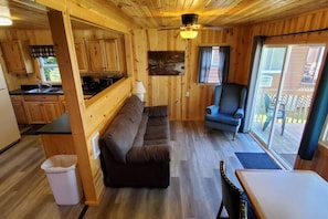 A wooden interior with a sofa, a chair, a table, and a kitchen area.