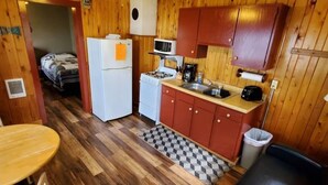 A compact kitchen with wooden walls, a refrigerator, a microwave, a stove, and a sink.