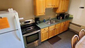 A compact kitchen with wooden cabinets, a refrigerator, a stove, a microwave, and a sink.