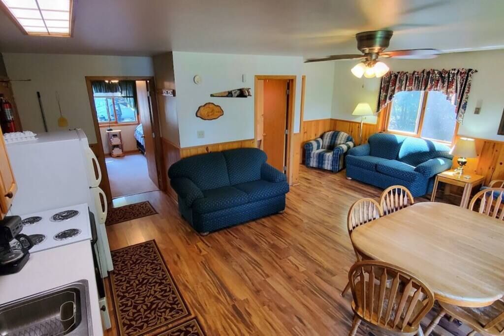A cozy living room with a blue sofa, a dining table with chairs, a kitchen area with a stove, and a ceiling fan.