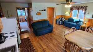 A cozy living room with a blue sofa, a dining table with chairs, a kitchen area with a stove, and a ceiling fan. - 2 Bedroom Wolf Villa in Voyageurs National Park (Kabetogama)