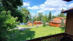 A wooden deck with a view of a grassy yard, several cabins, and a body of water in the background. - 2 Bedroom Wolf Villa in Voyageurs National Park (Kabetogama)