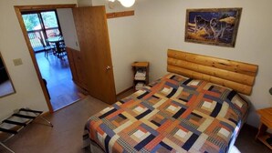 A bedroom with a wooden headboard, a quilted bedspread, a ceiling fan, a painting of wolves, and a door leading to a balcony. - 2 Bedroom Wolf Villa in Voyageurs National Park (Kabetogama)