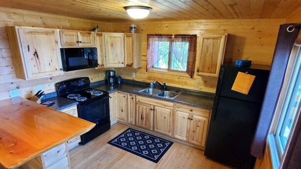Eine Holzhütte mit einer Küche, inklusive Herd, Mikrowelle, Spüle und Kühlschrank.