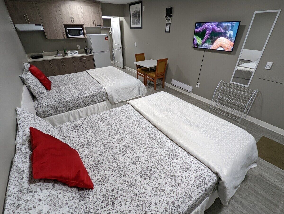 A hotel room with two beds, a small kitchenette, a TV, and a mirror.
