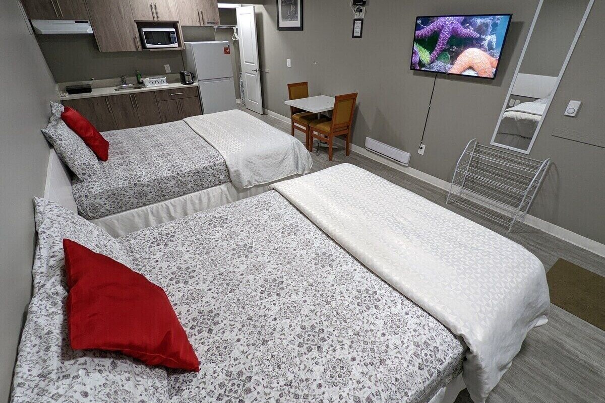 A hotel room with two beds, a small kitchenette, a TV, and a mirror.