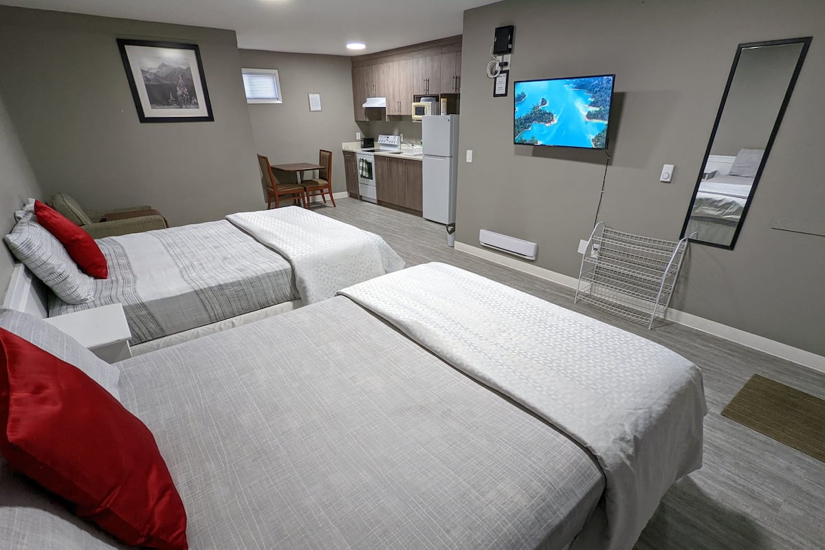 Quarto de hotel com duas camas, uma mesa de jantar, uma cozinha e uma televisão.
