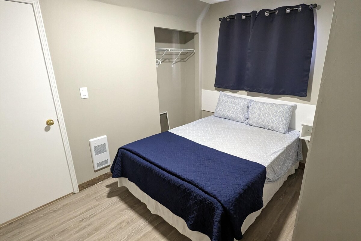 A bedroom with a bed, a wardrobe, a window with a curtain, and a vent.