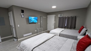 A hotel room with two beds, a television, a heater, and a window with curtains. - Riverside Motel & Suites (Medicine Hat)