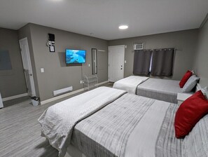 A hotel room with two beds, a television, a heater, and a window with curtains. - Riverside Motel & Suites (Medicine Hat)