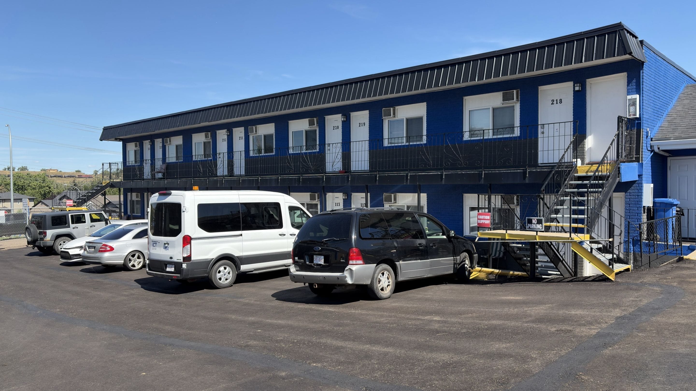 A parking lot with several cars and a building with numbered windows and a fire escape.