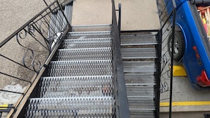 A metal staircase with a handrail leading to a concrete landing, adjacent to a blue vehicle. - Riverside Motel & Suites (Medicine Hat)