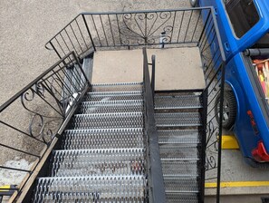 A metal staircase with a handrail leading to a concrete landing, adjacent to a blue vehicle. - Riverside Motel & Suites (Medicine Hat)