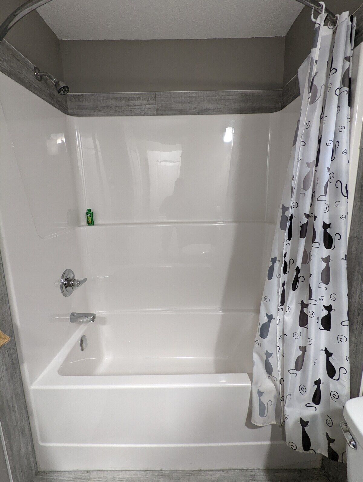 A bathroom with a white bathtub, a shower curtain with cat patterns, and a green bottle on the wall.