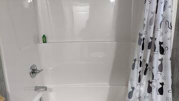 A bathroom with a white bathtub, a shower curtain with cat patterns, and a green bottle on the wall.