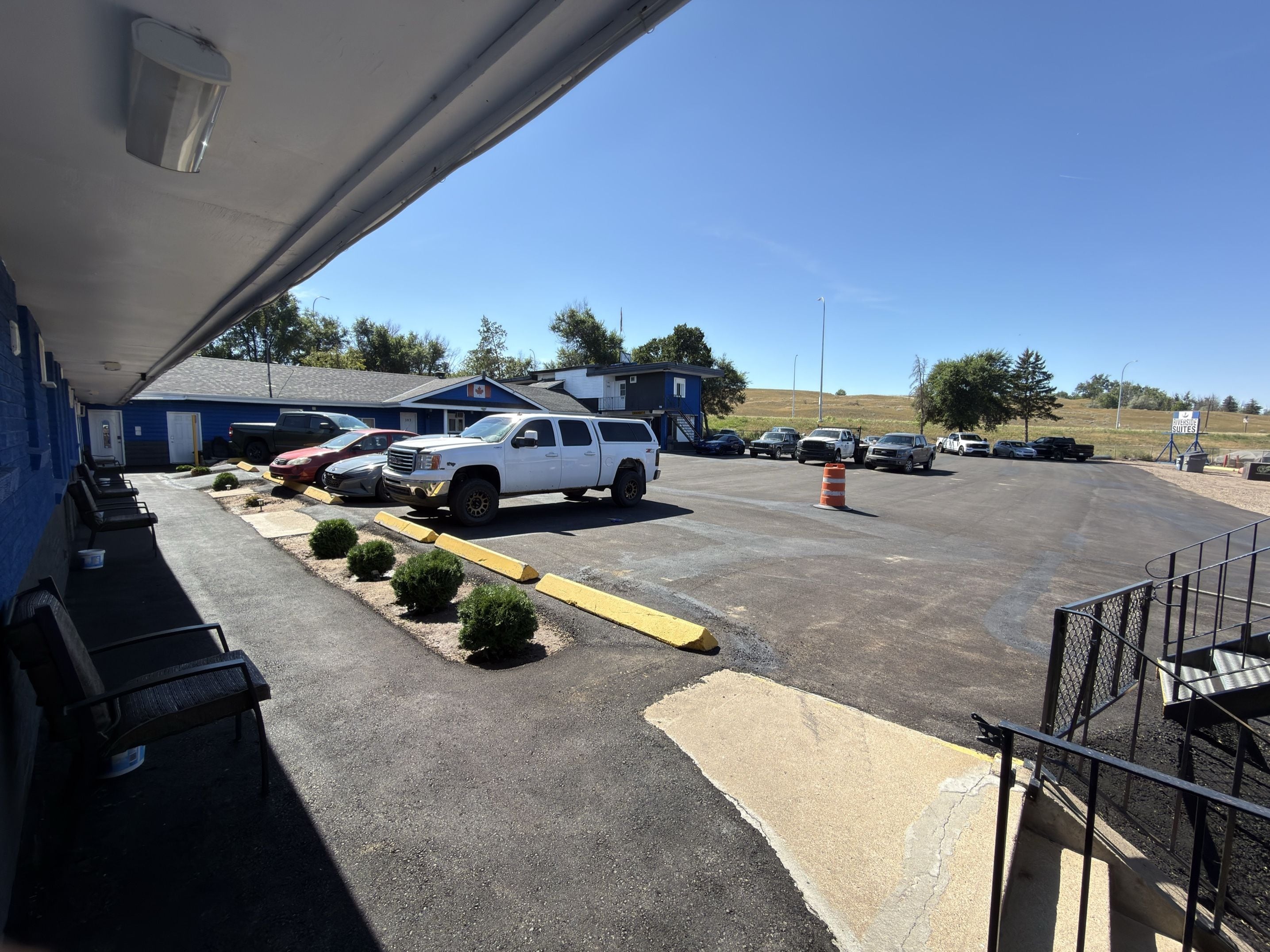 A parking lot with multiple vehicles, a building with a blue exterior, and a clear sky.