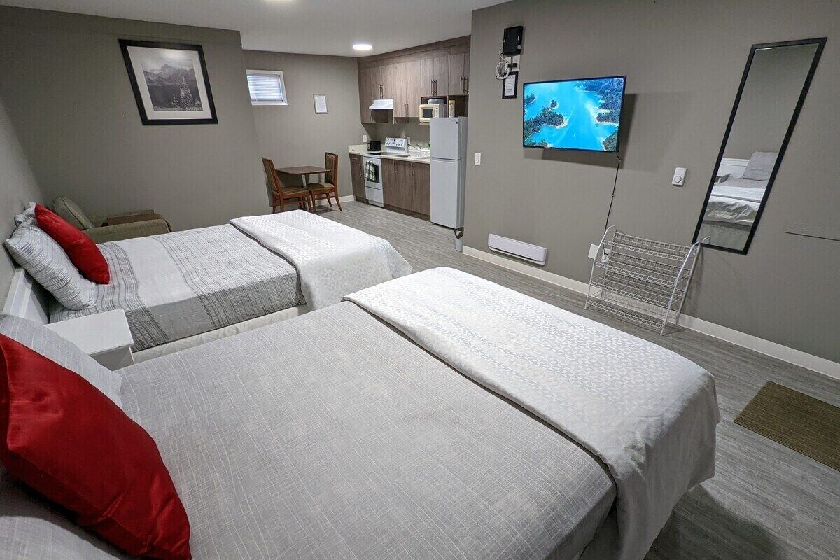 A hotel room with two beds, a kitchenette, a television, and a large mirror.
