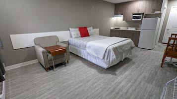 A hotel room with a bed, a chair, a small table, a microwave, a refrigerator, and a kitchenette.