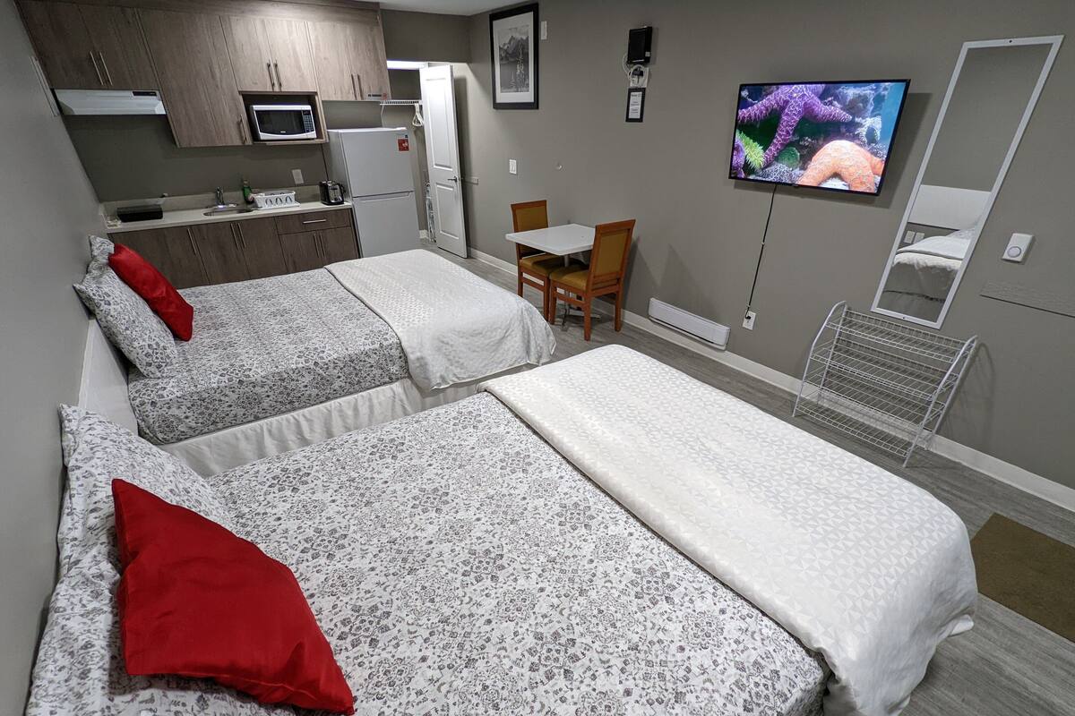 Quarto de hotel com duas camas, cozinha compacta, televisão e pequena área de refeições.