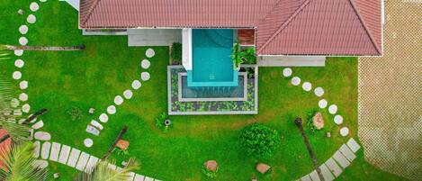 Vista aérea de una villa con piscina, rodeada de un jardín cuidado y un camino de piedra.