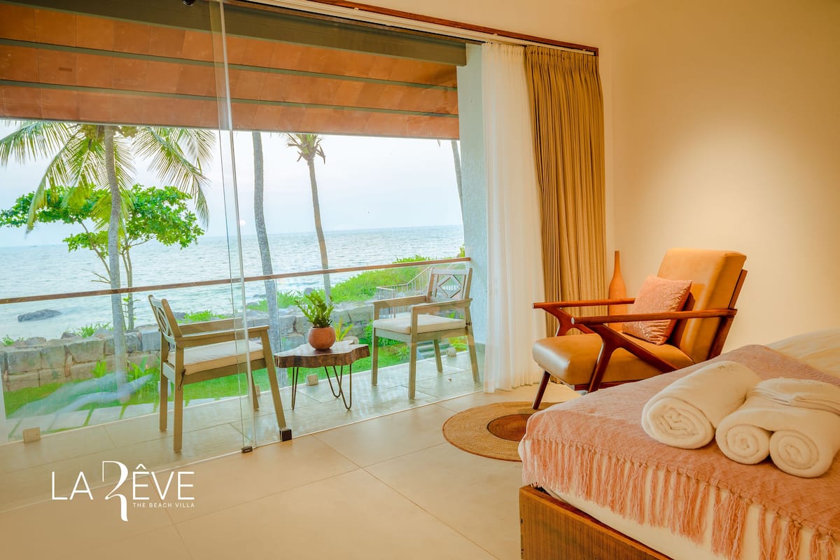 A hotel room with a large balcony, a bed with towels, a chair, and a table with a plant.
