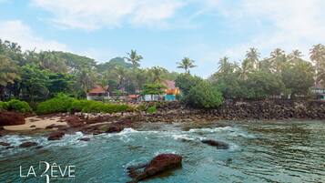 A beach view with rocky shoreline, palm trees, and a building with a red roof.