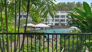 A pool area with umbrellas, a building with balconies, and lush greenery. - 1 Bedroom Ground Floor Pool Access Apartment 5114 (Palm Cove)