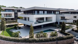 Un moderno edificio residencial de varios pisos con piscina, rodeado de jardines ajardinados y palmeras.