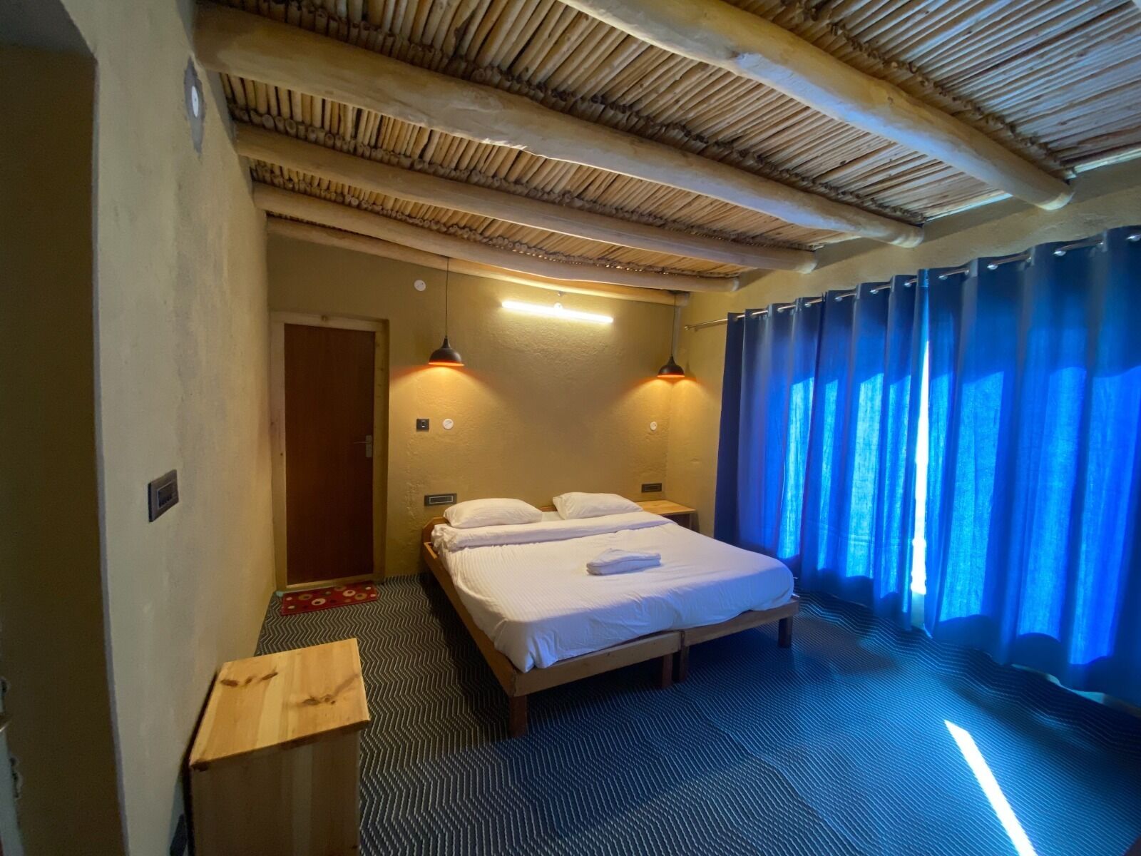 Une chambre avec un lit, deux lampes de chevet, une tête de lit en bois, un rideau bleu et une moquette à motifs.