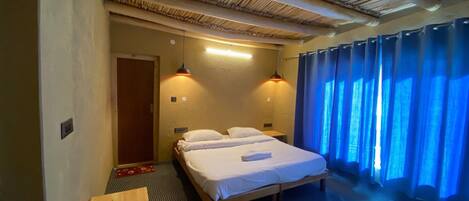 Une chambre avec un lit, deux lampes de chevet, une tête de lit en bois, un rideau bleu et une moquette à motifs.